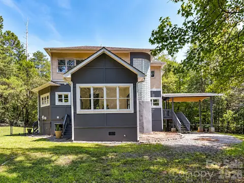 Rear view highlights the home’s distinctive architecture, expansive windows, covered outdoor living space, and private wooded backdrop.