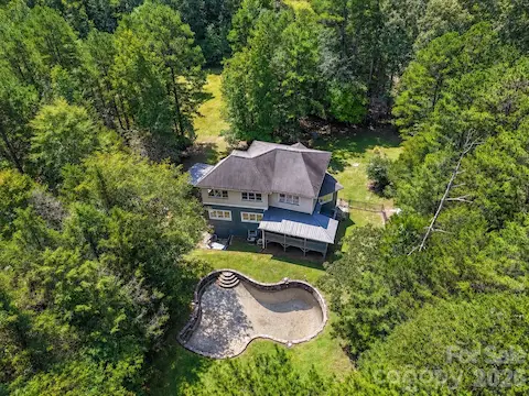 Aerial view showcases the private wooded setting, spacious backyard, and in-ground pool area surrounding the home.