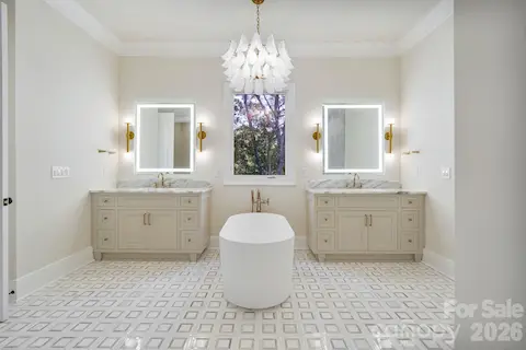 Spa-inspired primary bath featuring separate his-and-hers vanities, a sculptural freestanding tub with statement lighting, luxury illuminated mirrors, and a large window that fills the space with natural light.