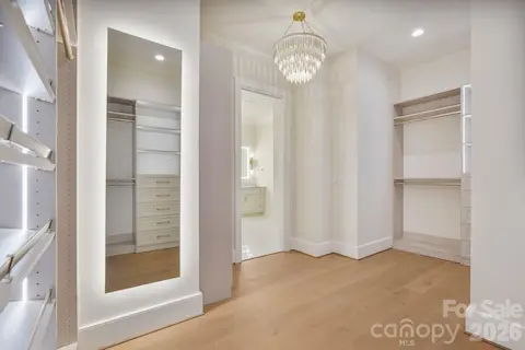 Boutique-inspired primary closet featuring oversized LED mirrors, custom built-ins, and a statement light fixture, creating an elevated space designed for getting ready in style.