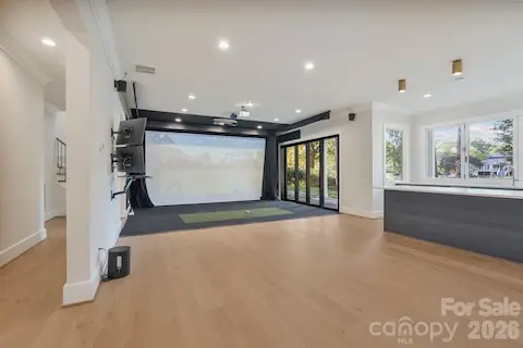 Open view of the golf simulator and entertainment space, featuring a quad-stack sliding glass door that opens to the covered porch for seamless indoor-outdoor living.