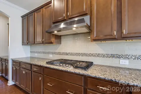 A gas cooktop, vent hood, and expansive counter space give the kitchen a practical, well-equipped workspace.
