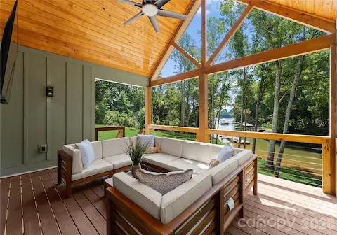 Exposed timber beams and a vaulted wood ceiling give this covered porch a warm, inviting feel, with views through the trees toward the water.