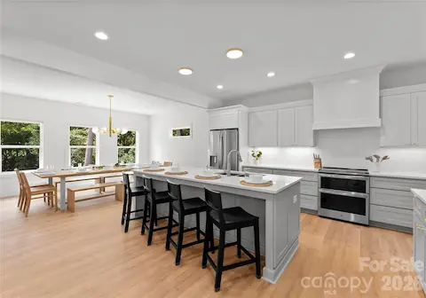A spacious island anchors the kitchen, with seating for casual meals and a dining area framed by views of the trees.