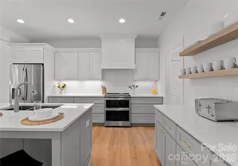 Light cabinetry, open wood shelving, and sleek countertops give the kitchen a clean, polished look with plenty of space to prepare and serve.