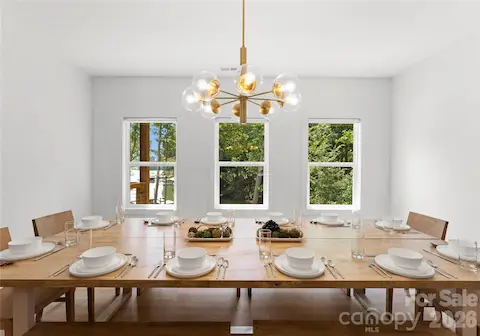 Gather around the spacious dining table beneath a statement chandelier, with views of the trees and water beyond.