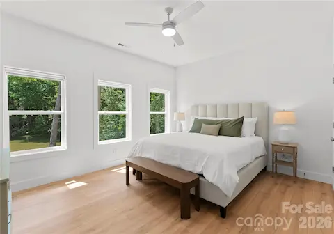Three windows fill this spacious bedroom with natural light and views of the wooded grounds.