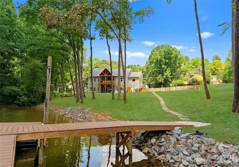 A path crosses the broad lawn from the shoreline to the home, with the covered porch and pool beyond.